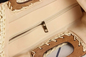 Detail view of woven straw handbag featuring wood handles, beige lining, and zipper pocket