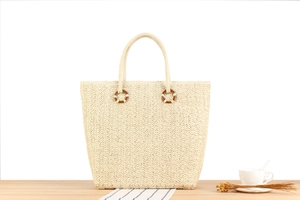 Détail d'un sac cabas en paille beige avec tissage en V et boucle en bois sur bois
