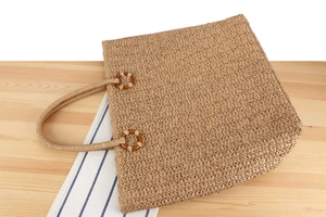 Détail du sac cabas en paille avec anneaux en bois sur une table d'été légère