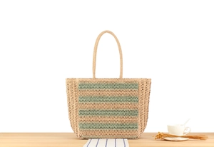 Close-up of woven straw beach bag with green stripes and detailed texture on wood surface