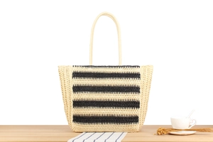 Detail of hand-woven straw tote bag with black stripes on a wooden table surface