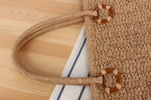 Détail du sac cabas en paille tressée avec anneau décoratif en bois brun sur l'anse