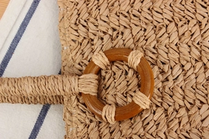 Détail d'un sac cabas en paille avec un anneau de poignée en bois foncé sur le côté