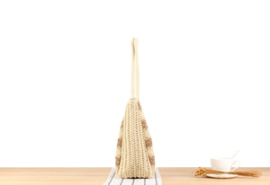 Detail of striped woven tote bag showing side structure and braided texture on table