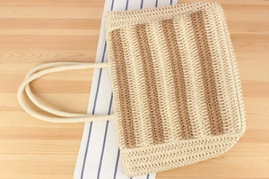 Top view of a woven straw tote bag with horizontal stripes on a rustic wooden table