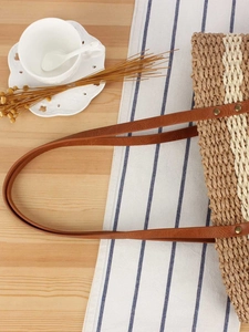Sac fourre-tout en paille tressée marron et beige avec anses en cuir sur une table