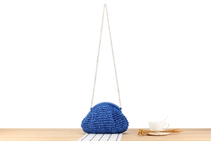 Detail of royal blue woven seashell bag with a slim gold chain on a wooden table