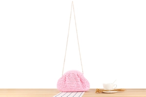 Detail of pink hand-woven crochet bag with a sleek gold chain strap on a wooden table