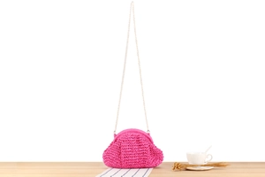Detail of fuchsia hand-woven crochet bag with premium gold chain strap on a wooden desk