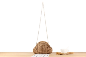 Macro view of woven crochet texture and gold chain on the khaki straw crossbody bag