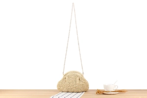 Detail of a beige woven dumpling bag with a delicate gold chain on a wooden table