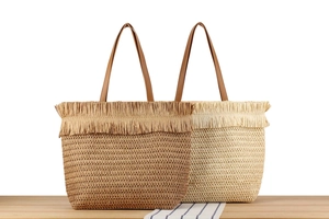 Detail of woven straw tote bags in beige and brown with fringe trim on a striped cloth