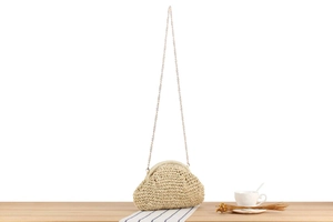 Detail of hand-woven cloud-shaped crossbody bag with gold chain strap on a wooden table