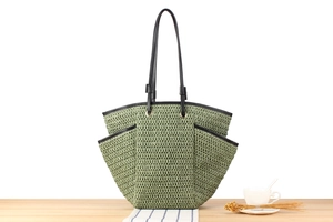 Detail of green woven tote bag featuring multiple pockets and black leather shoulder straps