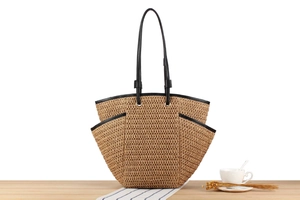 Detail of woven straw tote bag featuring a side pocket and black trim on a wooden table