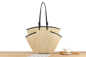 Detail of hand-woven straw tote bag with black trim on a natural wooden table