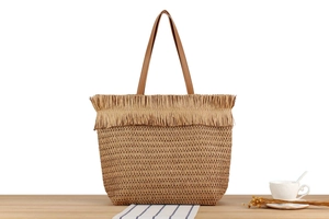 Close-up of woven straw tote bag featuring decorative fringe trim and brown leather handles