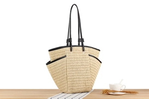 Detail of beige hand-woven straw tote bag with black leather straps on a wooden table