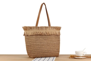 Close-up of woven straw tote bag featuring raffia fringes and brown leather straps