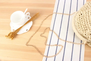 Detail of round straw shoulder bag with metallic chain on warm wood background