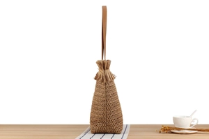 Detail view of woven straw tote bag with fringe tassels and brown leather straps