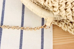 Detail of woven straw bag with golden metal chain strap and fine stitching texture
