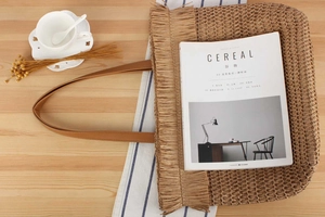 Detail view of woven straw tote bag with fringe edge and leather handles on wooden table