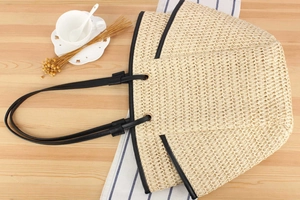 Detail of woven straw tote bag with black leather straps on a wooden table setup