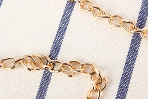 Detailed macro view of a glossy gold metal chain accessory on a striped fabric surface