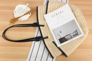 Detail of hand-woven straw tote with black leather handles on a lifestyle table setup