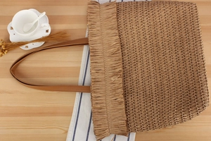 Detail of woven straw tote bag with fringe accents on a rustic wood tabletop setting