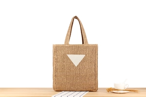 Detailed view of woven straw tote bag texture and white triangle patch on wooden table