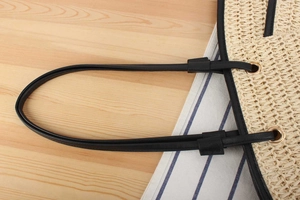 Detail of woven straw tote bag featuring black leather handles and gold metal hardware