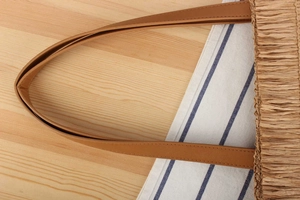 Detail shot of woven straw bag showing quality stitching on brown leather handle
