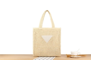Detail of a woven cream straw tote bag featuring a triangular patch on a wooden desk