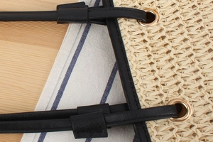 Macro shot of hand-woven straw tote featuring black leather trim and gold eyelets