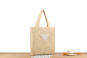 Detail of hand-woven beige straw tote bag with triangular patch on a wooden table