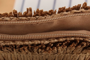 Macro detail of high-quality zipper closure and woven straw texture on a fringe tote bag