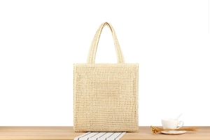 Detail of hand-woven straw tote bag with dual handles on a wooden table setup
