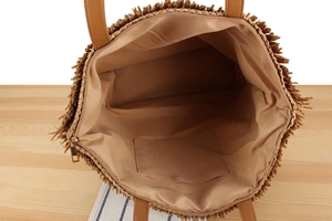 Detail view of woven straw tote bag with inner lining, zipper pocket and tassel edges