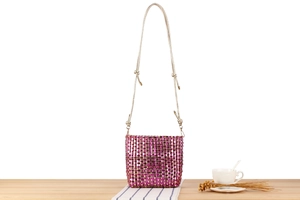 Close-up of woven purple and gold bucket bag on a wooden table with home decor