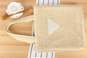 Detailed top view of a woven straw tote bag in cream on a wooden desk with a coffee cup