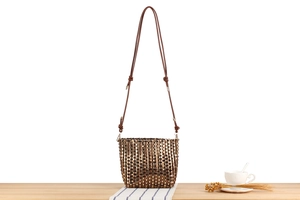 Detail of woven crossbody bag showing intricate brown and metallic grid texture and leather strap