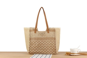 Detail einer gewebten Stroh-Tote-Bag mit braunen Ledergriffen auf einem Holztisch