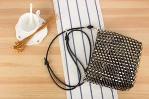 Detailed close-up of a black and gold woven crossbody bag on a natural wooden table