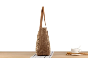 Detail einer braunen Strohtasche mit weißem Häkelblumenmuster und Lederriemen