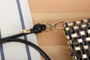 Detail of woven handbag featuring black and gold beads with metallic carabiner attachment