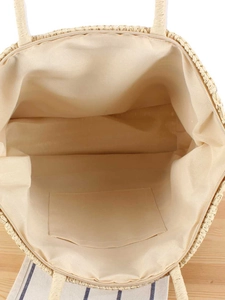 Large beige woven straw tote bag with zipper closure and interior pocket on a wooden desk