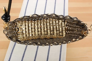 Detailed top view of the woven handbag with gold beads and black leather strap