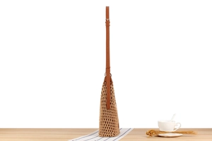Close-up of beige woven shoulder bag with brown leather strap on a wooden table